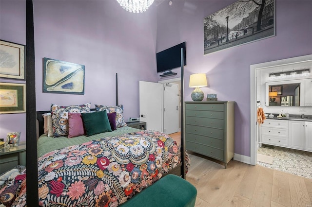 bedroom featuring a notable chandelier, a high ceiling, ensuite bathroom, a sink, and light wood-type flooring