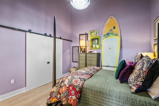 bedroom with wood finished floors, baseboards, an inviting chandelier, and a barn door