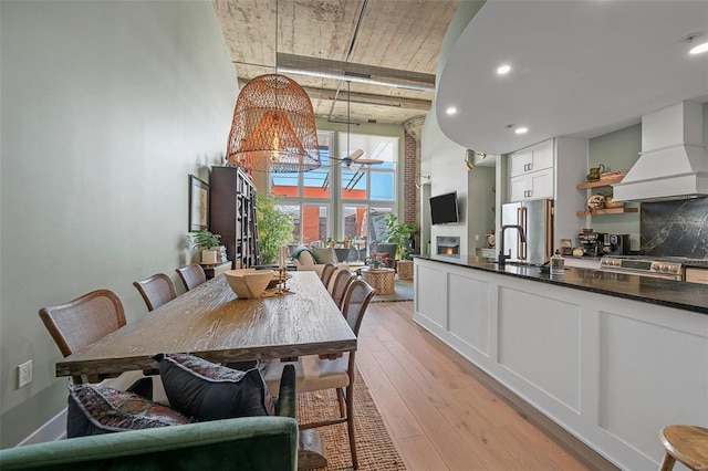 dining space with light wood-type flooring, an inviting chandelier, a lit fireplace, and a towering ceiling