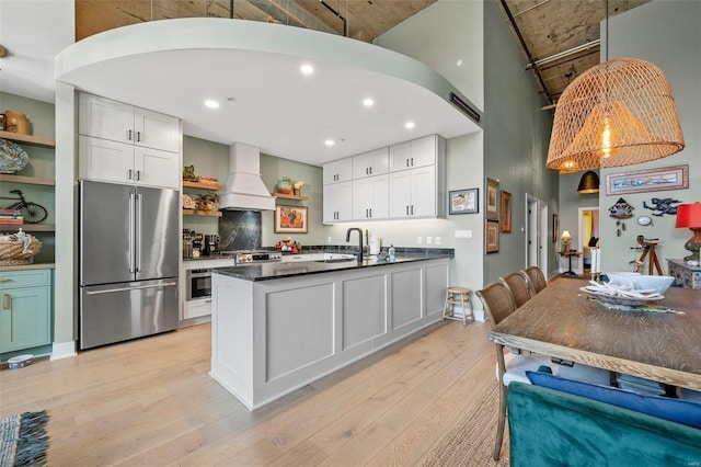 kitchen featuring premium range hood, high end refrigerator, light wood-type flooring, open shelves, and dark countertops