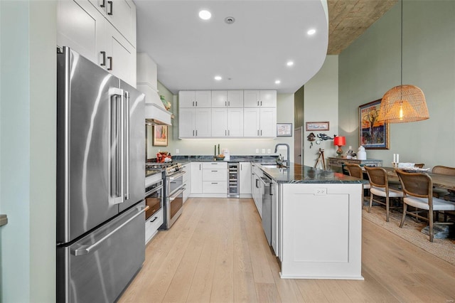 kitchen featuring beverage cooler, a peninsula, premium range hood, appliances with stainless steel finishes, and light wood-type flooring