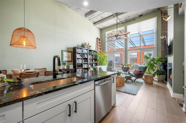 kitchen with pendant lighting, light wood-style flooring, a towering ceiling, stainless steel dishwasher, and a sink