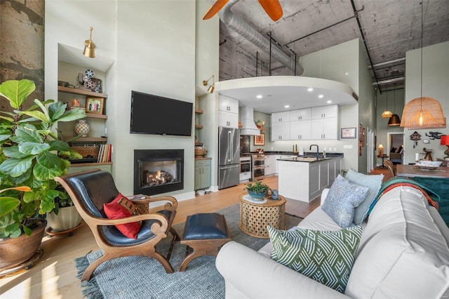 living area featuring a warm lit fireplace, arched walkways, a towering ceiling, a ceiling fan, and light wood-type flooring