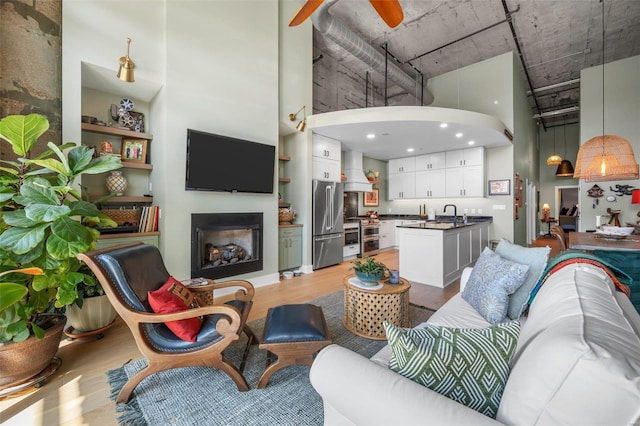 living room with arched walkways, a towering ceiling, ceiling fan, light wood-type flooring, and a fireplace