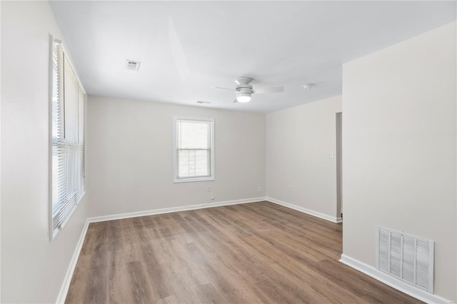 unfurnished room with ceiling fan, wood finished floors, visible vents, and baseboards