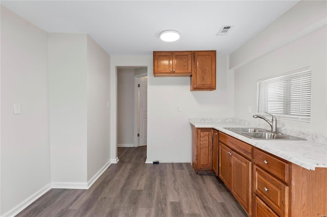 kitchen featuring dark wood-style floors, brown cabinetry, a sink, and light countertops