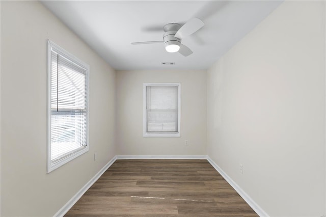 empty room featuring dark wood-style floors, a ceiling fan, visible vents, and baseboards