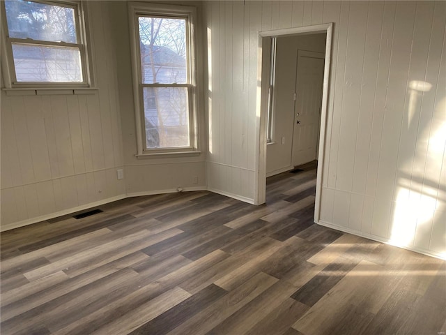 spare room with dark wood-style floors, visible vents, and baseboards