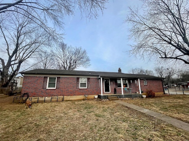 single story home featuring a porch, a chimney, a front lawn, and brick siding