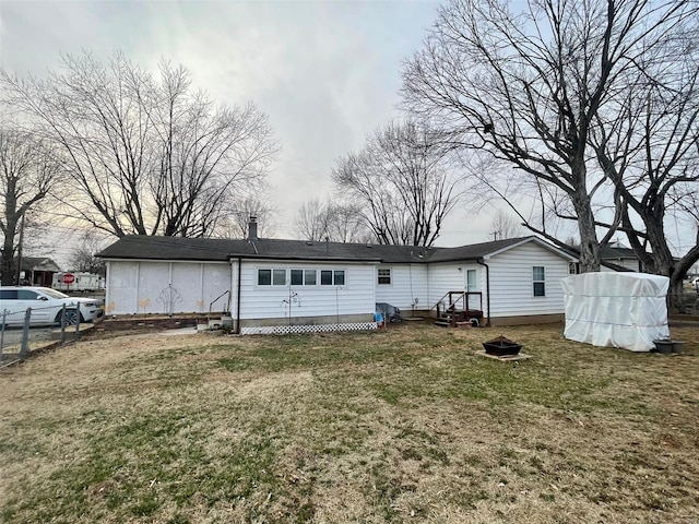 back of house featuring a fire pit, fence, and a lawn