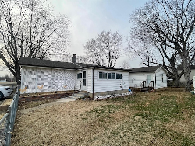 back of house featuring entry steps, a chimney, fence, and a lawn