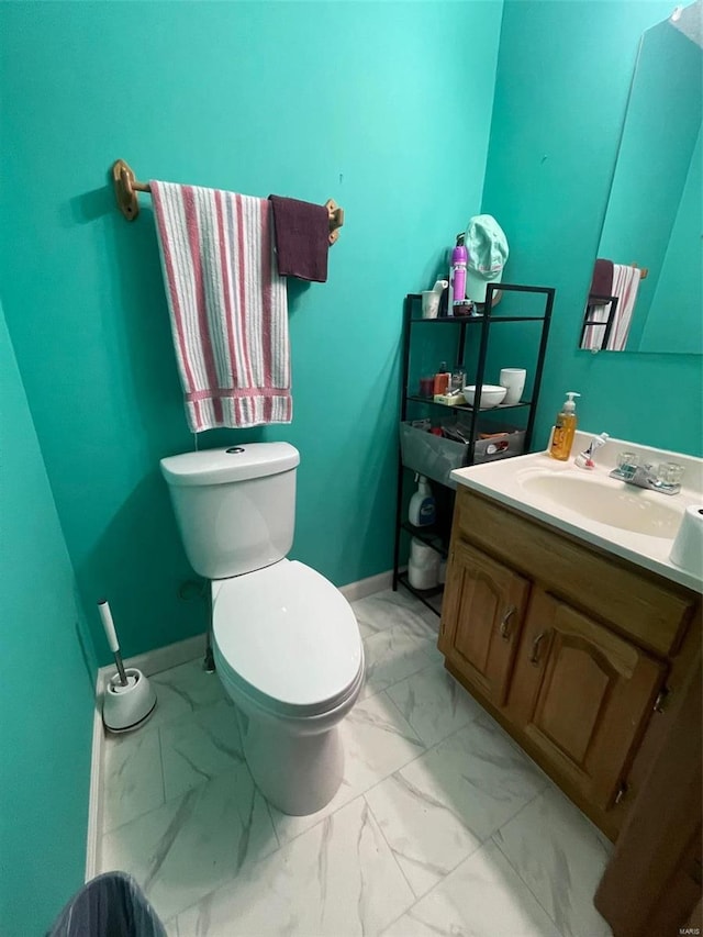 half bath with toilet, marble finish floor, baseboards, and vanity