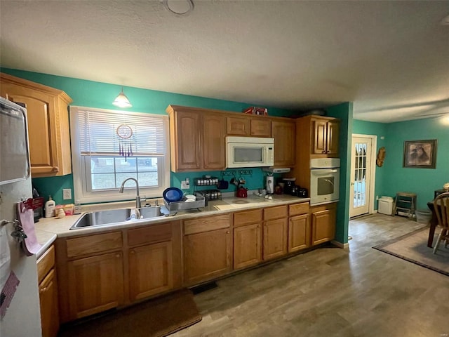 kitchen featuring light countertops, white microwave, a sink, light wood-type flooring, and oven