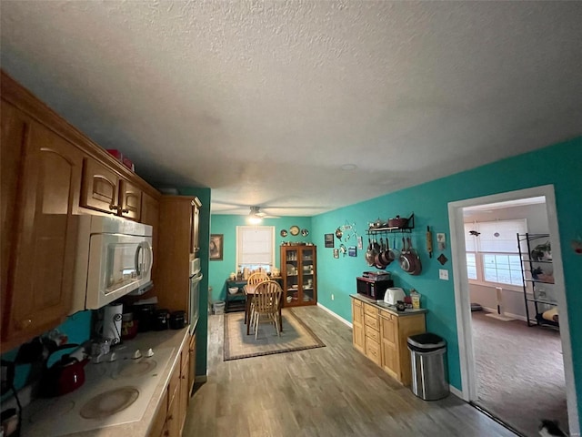 kitchen featuring a textured ceiling, black microwave, white microwave, baseboards, and light wood-type flooring