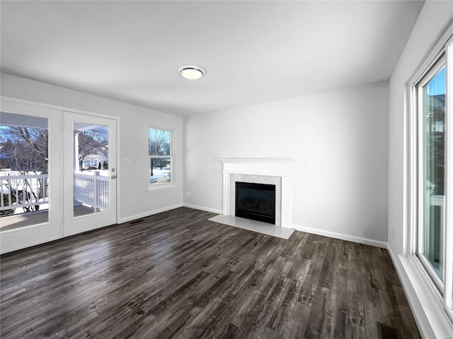 unfurnished living room featuring dark wood-style flooring, a high end fireplace, visible vents, and baseboards