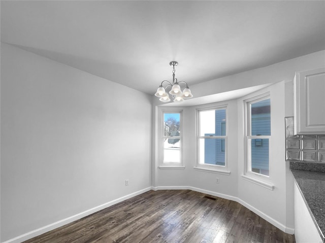 unfurnished dining area with baseboards, visible vents, a chandelier, and dark wood-type flooring