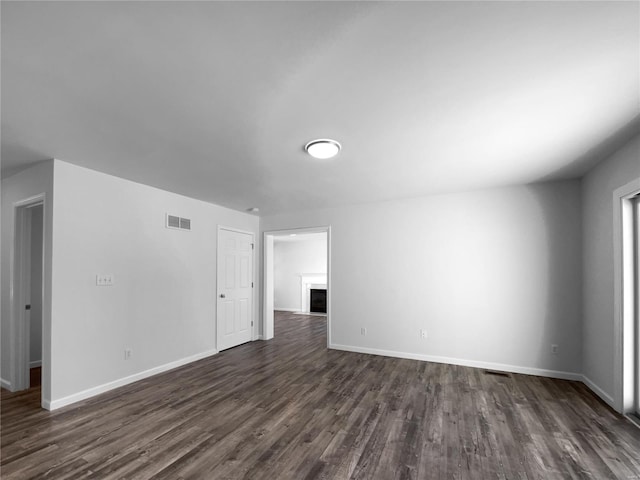 spare room featuring dark wood-style flooring, visible vents, a fireplace, and baseboards