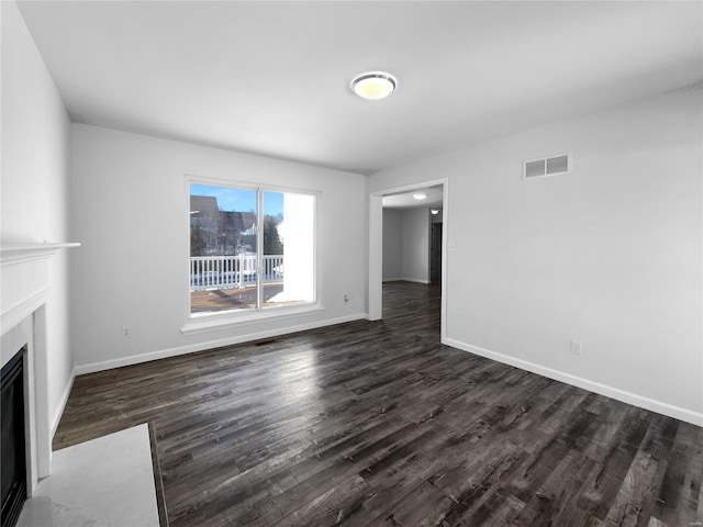 unfurnished living room with dark wood-type flooring, a fireplace with flush hearth, visible vents, and baseboards