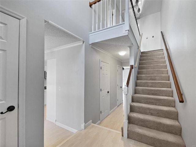 staircase featuring a textured ceiling, baseboards, crown molding, and wood finished floors