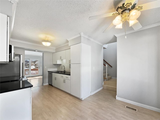 kitchen featuring visible vents, dark countertops, crown molding, white cabinetry, and a sink