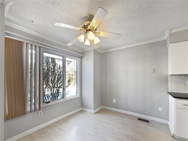 unfurnished dining area featuring light wood-style floors, a textured ceiling, baseboards, and crown molding