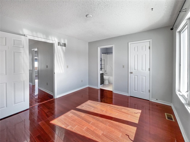 unfurnished bedroom with a textured ceiling, wood finished floors, visible vents, and baseboards