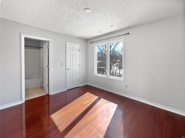 unfurnished bedroom with a textured ceiling, wood finished floors, visible vents, baseboards, and ensuite bath