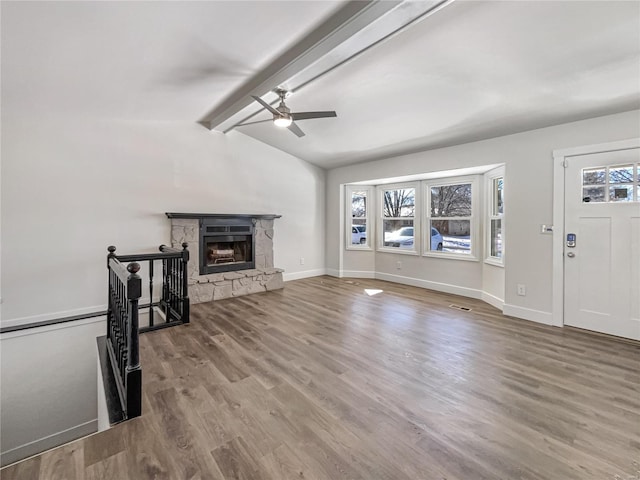 living area with lofted ceiling with beams, a stone fireplace, baseboards, and wood finished floors