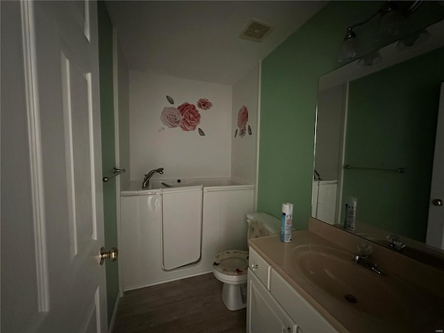 bathroom with visible vents, toilet, wood finished floors, a garden tub, and vanity