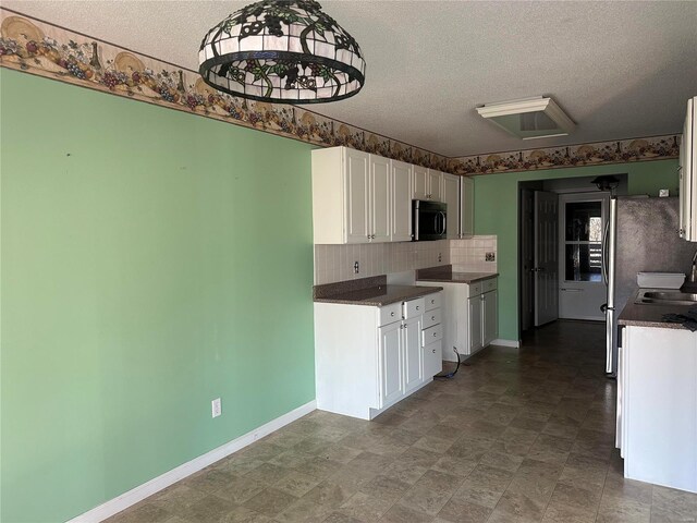 kitchen with dark countertops, stainless steel microwave, decorative backsplash, white cabinets, and a textured ceiling