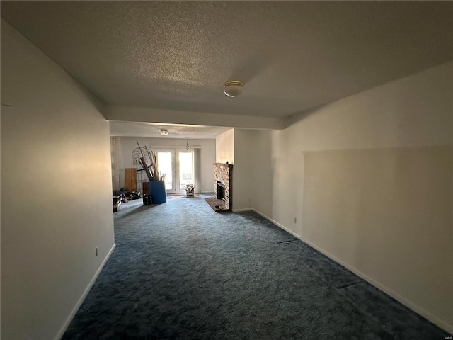 interior space with baseboards, a fireplace with raised hearth, a textured ceiling, and dark colored carpet