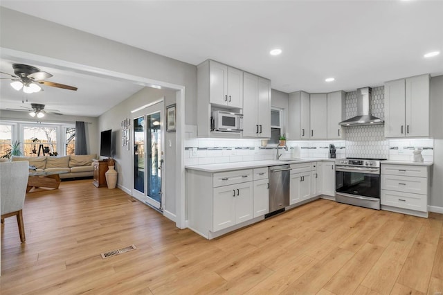 kitchen with visible vents, stainless steel appliances, light countertops, wall chimney range hood, and light wood-type flooring