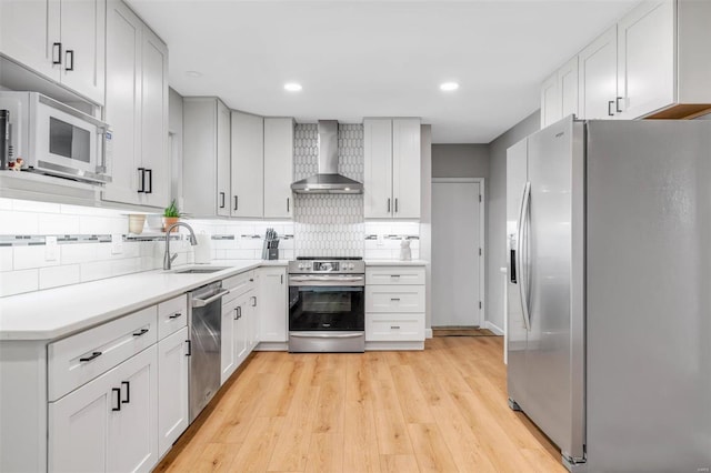 kitchen featuring light wood-type flooring, a sink, tasteful backsplash, stainless steel appliances, and wall chimney exhaust hood