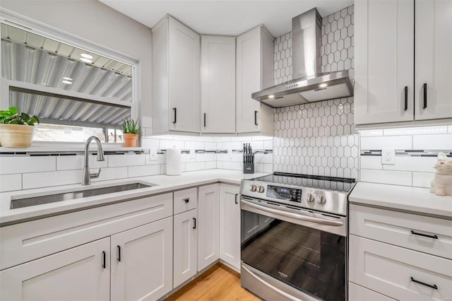 kitchen with tasteful backsplash, stainless steel electric stove, light countertops, wall chimney exhaust hood, and a sink