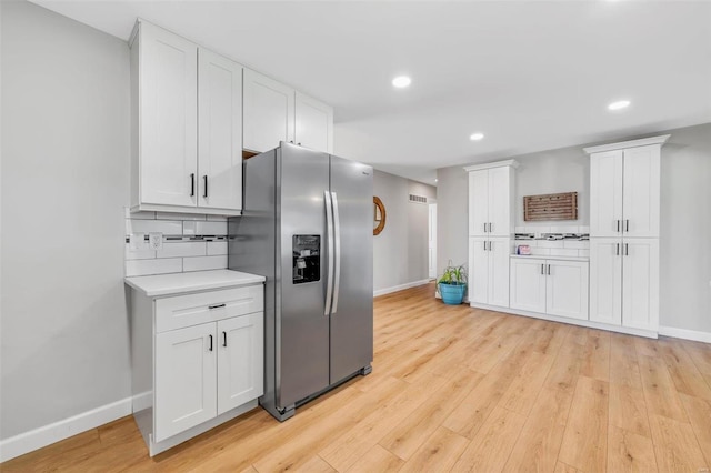 kitchen featuring tasteful backsplash, light countertops, light wood-style flooring, stainless steel refrigerator with ice dispenser, and white cabinets