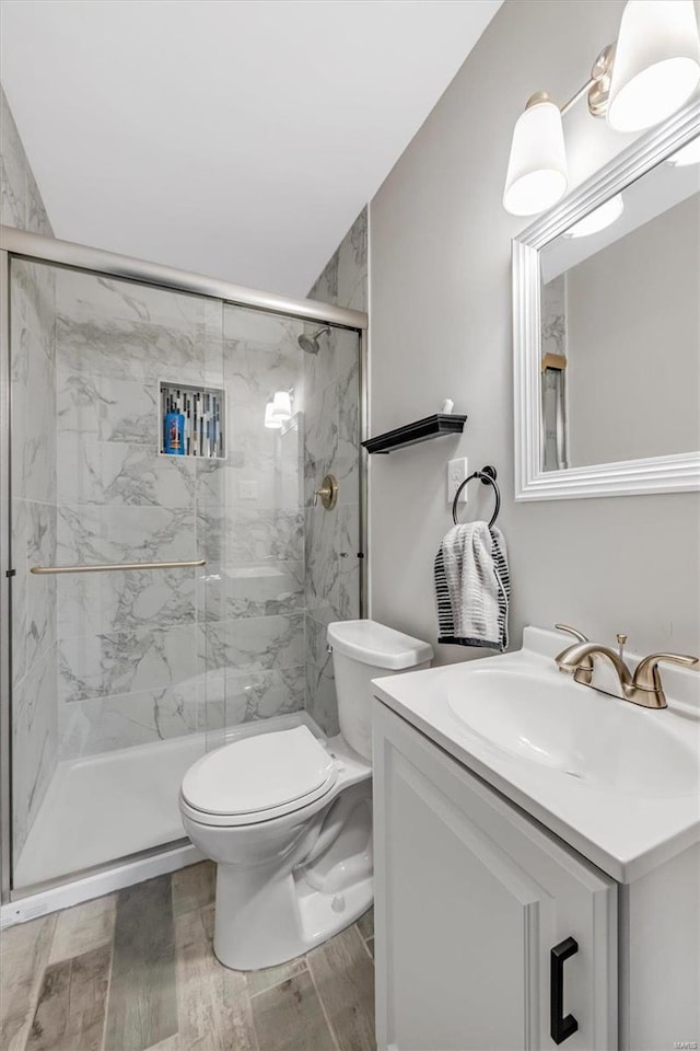 full bathroom featuring a marble finish shower, toilet, vanity, and wood finish floors