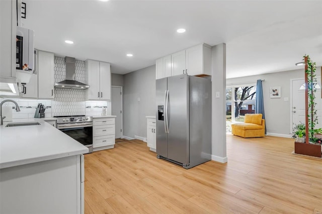 kitchen featuring light wood finished floors, a sink, decorative backsplash, appliances with stainless steel finishes, and wall chimney range hood