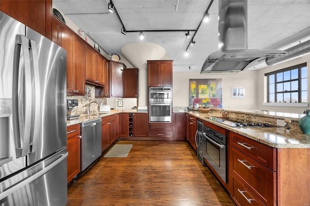 kitchen featuring island exhaust hood, stainless steel appliances, dark wood-type flooring, light stone countertops, and a peninsula