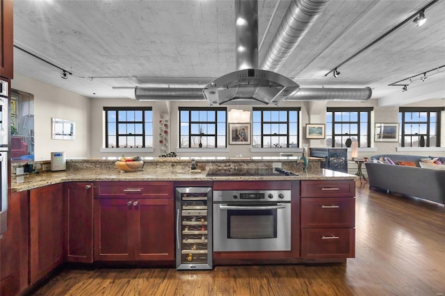 kitchen with reddish brown cabinets, beverage cooler, stainless steel oven, and black electric stovetop