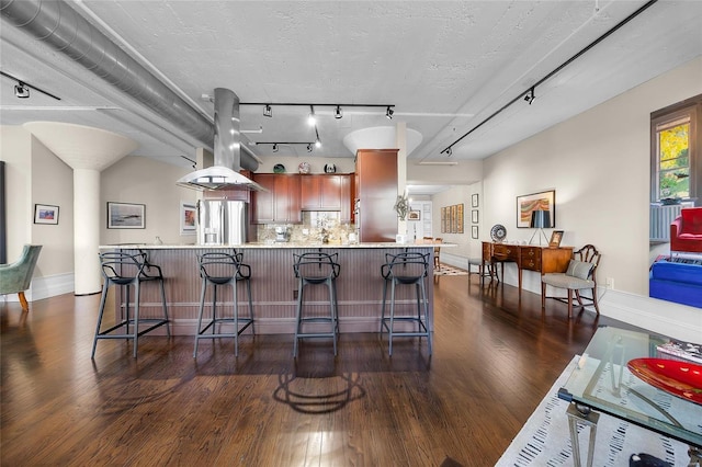 kitchen featuring island range hood, light countertops, decorative backsplash, dark wood-style floors, and stainless steel fridge