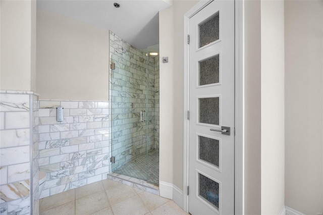 bathroom with a wainscoted wall, a shower stall, tile walls, and tile patterned floors