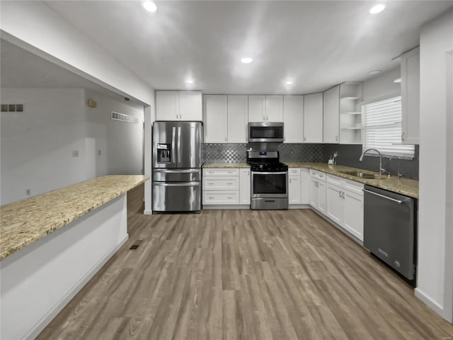 kitchen with light wood finished floors, open shelves, appliances with stainless steel finishes, white cabinets, and a sink