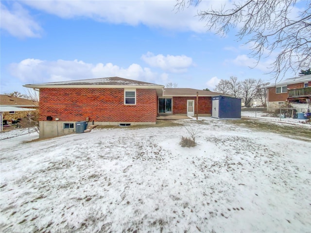 snow covered house with central AC, brick siding, and fence