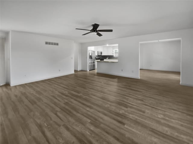 unfurnished living room featuring ceiling fan, dark wood finished floors, visible vents, and baseboards