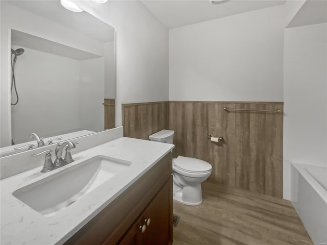 bathroom featuring toilet, a wainscoted wall, wood finished floors, vanity, and a bath