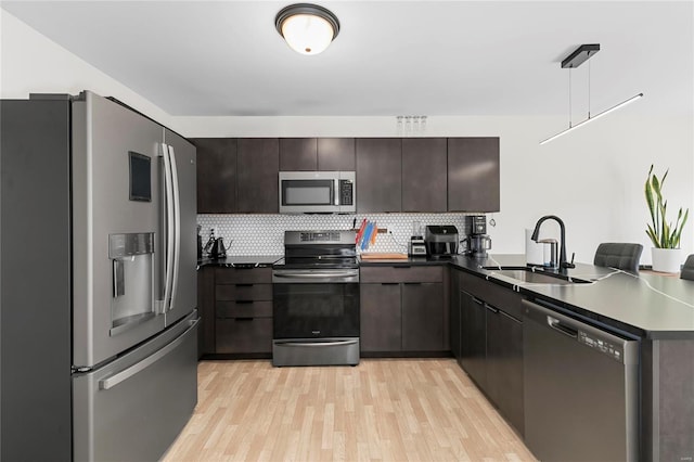 kitchen featuring decorative backsplash, dark countertops, stainless steel appliances, light wood-style floors, and a sink