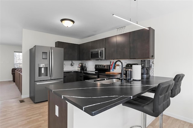 kitchen with a peninsula, tasteful backsplash, appliances with stainless steel finishes, and a kitchen breakfast bar