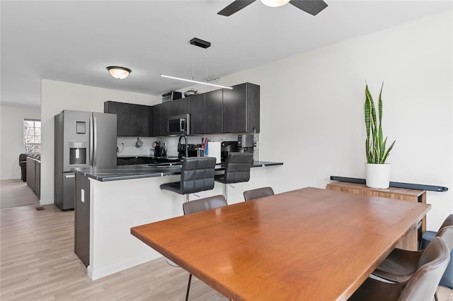 kitchen with light wood-style flooring, decorative backsplash, appliances with stainless steel finishes, dark cabinetry, and a peninsula