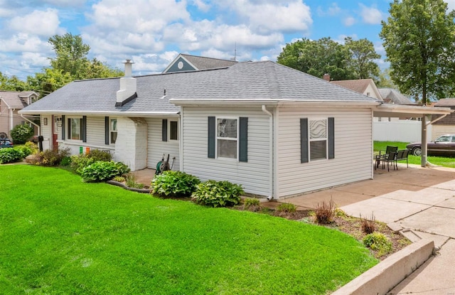 back of property featuring a chimney, a shingled roof, a lawn, and a patio area