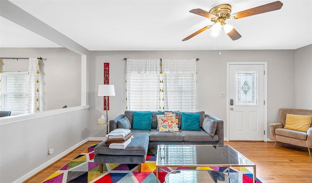 living area with a wealth of natural light, ceiling fan, baseboards, and wood finished floors